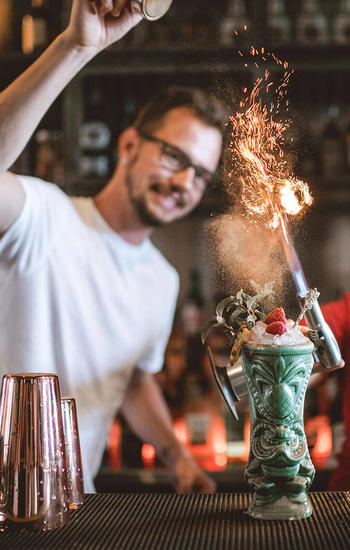 male bartender pouring cinnamon on tiki cocktail fire